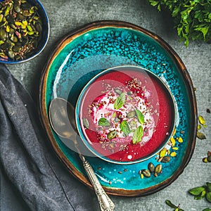 Spring beetroot soup on bright blue plate over gery background