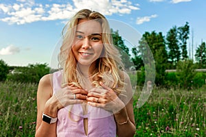 Spring blonde in nature with green grass with deep cleavage covers her chest with her hands