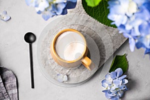 Spring bouquet with blue hydrangea flowers and a cup of cappuccino coffee in a yellow cup and spoon on a light background. The