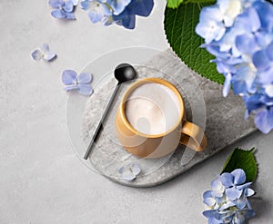 Spring bouquet with blue hydrangea flowers and a cup of cappuccino coffee in a yellow cup and spoon on a light background. The