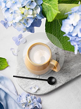 Spring bouquet with blue hydrangea flowers and a cup of cappuccino coffee in a yellow cup and spoon on a light background. The