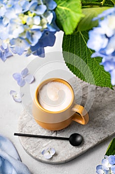 Spring bouquet with blue hydrangea flowers and a cup of cappuccino coffee in a yellow cup and spoon on a light background. The