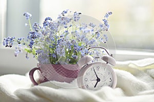 Spring bouquet of flowers and a cozy white plaid on the windowsill. pink clock by the window shows morning time