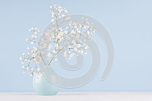 Spring bouquet of white small fluffy flowers in blue smooth circle ceramic vase on soft white wood table and pastel blue wall.