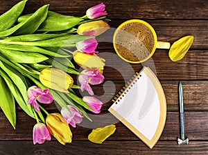 Spring bouquet of yellow and pink tulips, white cup of coffee, colorful notebook, pen
