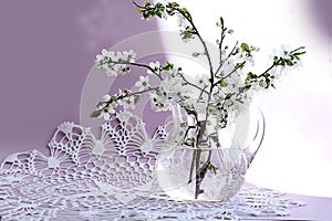 Spring bouquets: flowering branches in a glass jug on an openwork napkin