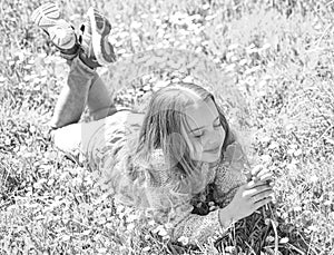 Spring break concept. Child enjoy spring sunny day while lying at meadow with daisy flowers. Girl on smiling face holds