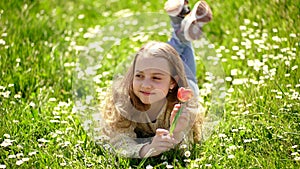 Spring break concept. Child enjoy spring sunny day while lying at meadow with daisy flowers. Girl on smiling face holds