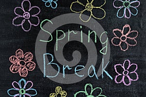 Spring break with flowers written in colorful chalk on black chalkboard