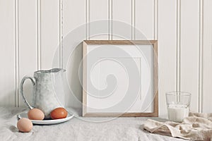 Spring breakfast still life scene. Square empty wooden frame mockup with chicken eggs,, glass of milk and ceramic jug