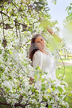 Spring brunette girl standing outdoor in blooming trees. Beautiful romantic woman in apple flowers. Young woman enjoying nature.