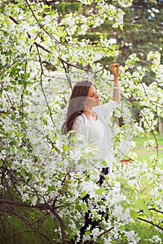 Spring brunette girl standing outdoor in blooming trees. Beautiful romantic woman in apple flowers. Young woman enjoying nature.