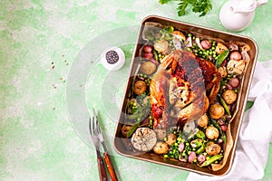 Spring chicken baked with radishes and green peas in one-pot on a green background.