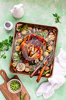 Spring chicken baked with radishes and green peas in one-pot on a green background.