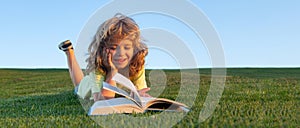 Spring and child. Banner for website header. Child boy reading book, laying on grass in field on sky background.