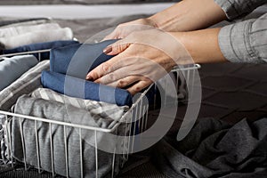 Spring cleaning of closet. Vertical tidying up storage. Neatly folded clothes in the metal white baskets for wardrobe. Grey