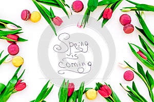 Spring is coming hand lettering surrounded by red tulips and sweets macarons on white background top view