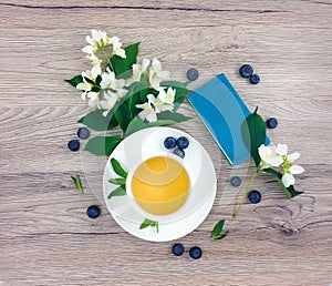 Spring composition of cup of tea, notebook and flowers on wooden table, flat lay