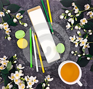 Spring composition of cup of tea, sketchbook and flowers on stone marble table, flat lay