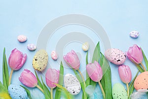 Spring composition with pink tulip, colorful eggs and feathers on blue table top view. Happy Easter card.