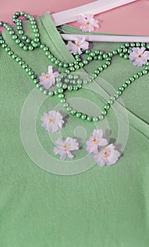 Spring concept with beautiful green sweater and pink flowers and pearls over pink backgrund