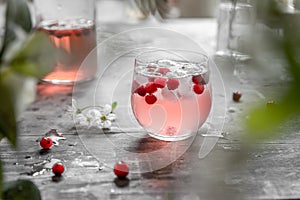 Spring cranberry lemonade in a glass on a gray shabby table with cherry flowers and leaves