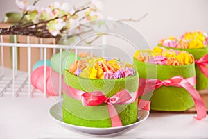 Spring Easter festive table. Small green cakes with butter cream flowers and colorful eggs on the background