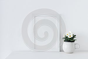Spring, Easter interior still life composition. Blank picture frame mockup on white table. White, yellow potted