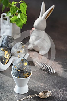 Spring Easter still life. White rabbit and eggs painted with gold pattern on a gray background.. Easter decor on the