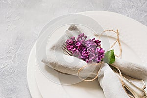 Spring elegant table place setting with violet lilac, silverware on vintage table. View from above.