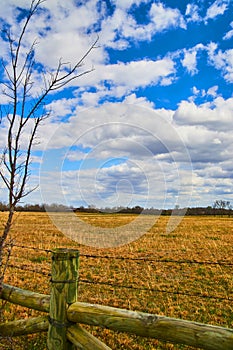 Spring farmland by wood fence and barbed wire with fluffy clouds and blue sky overhead