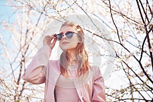 Spring fashion girl outdoors portrait in blooming trees. Beauty Romantic woman in flowers in sunglasses. Sensual Lady.