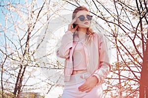 Spring fashion girl outdoors portrait in blooming trees. Beauty Romantic woman in flowers in sunglasses. Sensual Lady.