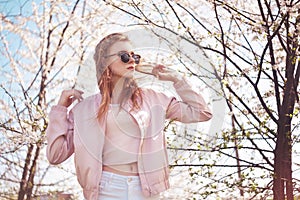 Spring fashion girl outdoors portrait in blooming trees. Beauty Romantic woman in flowers in sunglasses. Sensual Lady.