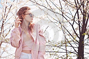 Spring fashion girl outdoors portrait in blooming trees. Beauty Romantic woman in flowers in sunglasses. Sensual Lady.