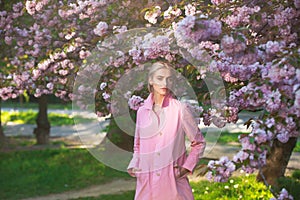 Spring fashion, girl in pink coat enjoy blossom sakura in garden. Flowers make women happy. Spring blossom. Tenderness