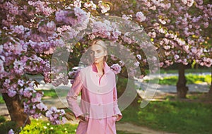 Spring fashion, girl in pink coat enjoy blossom sakura in garden. Flowers make women happy. Spring blossom. Tenderness