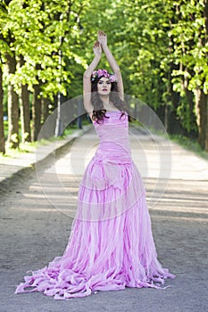 Spring fashion model woman with healthy hair and natural makeup wearing pink dress against green summer background outdoor