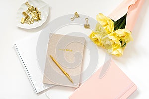 Spring Feminine workspace blogger. Notebooks with a pen, a bouquet of yellow tulips on a white background. Trendy stylish flat lay