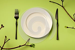 Spring festive table setting with white plate and black cutlery on a green background. Easter holiday creative concept. Branches
