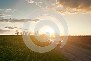 Spring field and car on dirt road at sunset