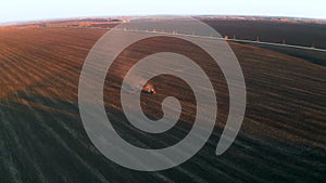 Spring field work, tractor cultivates land in the light of sunset, aerial video
