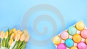 Spring flat lay with fresh yellow tulips colorful eggs on blue background.