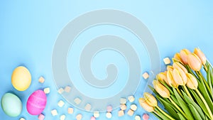 Spring flat lay with fresh yellow tulips colorful eggs on blue background. Easter, Mother day, birthday or Anniversary with copy-