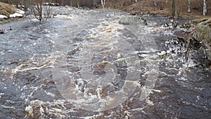 Spring flood. Rushing water in the river, top view. Dark ferrous water rushes in the stream. A yellow-white foam
