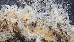 Spring flood. Rushing water in the river, top view. Dark ferrous water rushes in the stream. A yellow-white foam