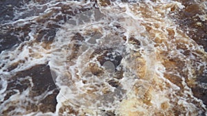 Spring flood. Rushing water in the river, top view. Dark ferrous water rushes in the stream. A yellow-white foam