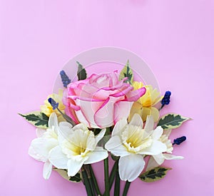 Spring flower arrangement. Yellow daffodils, pink astromeria and a large scarlet rose on a light pink background. photo