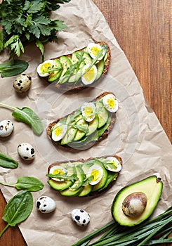 Spring food. A whole grain bread toast sandwiches with avocado, spinach, guacamole, arugula and quail eggs on parchment