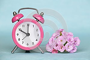 Spring forward, springtime, daylight saving time, pink alarm clock and flowers on a blue background